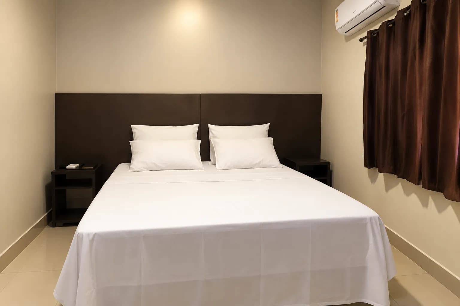 Cama de casal arrumada com lençóis brancos e cortina vinho